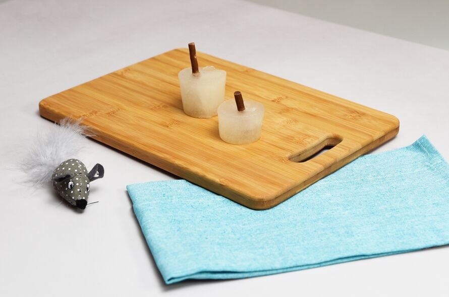 ice lolly with cat treat for the stick, standing on a board, on top of a blue tea towel