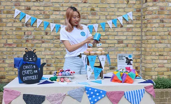 A person standing behind a cake and crafts sale